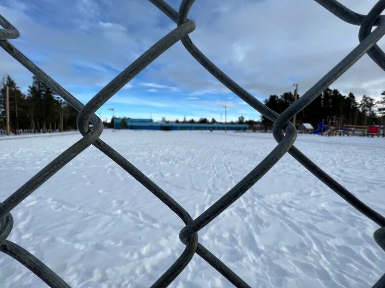 Across a snowy school yard, a low-lying elementary school painted two tones of blue is seen through a chain-link fence.