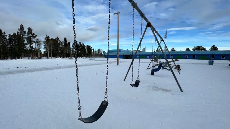 A swing set is seen in the snowy school yard of an elementary school painted in two tones of blue.