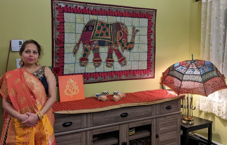 A woman in traditional Indian dress looks at the camera with a backdrop of a colourful piece of elephant artwork. 