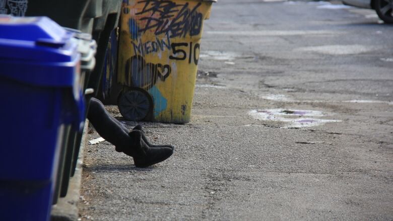 A person's legs are seen behind a garbage can. They're sitting on the side of a downtown street. 