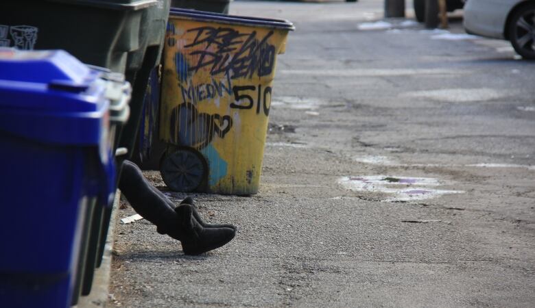 A person's legs are seen behind a garbage can. They're sitting on the side of a downtown street. 