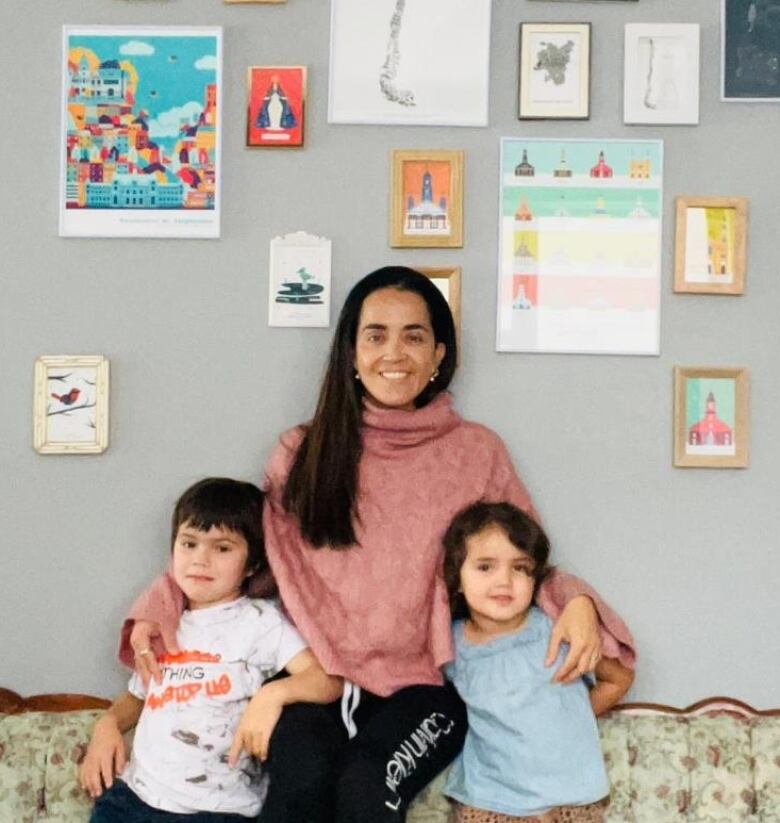 A woman and her two children pose against a wall of picture frames. 