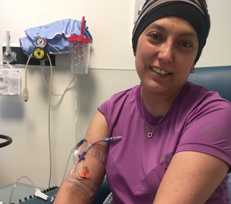 A woman with a head covering smiles for the camera but has an IV needle in her arm.