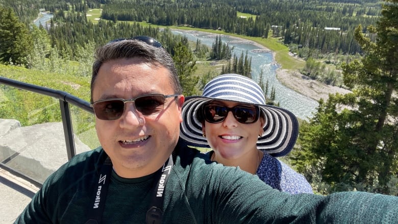 Two people stand together in front of a river in Kananaskis.