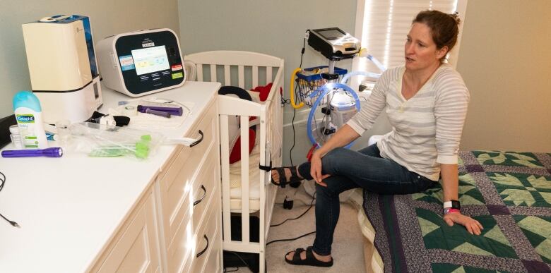 A woman sits on a bed near a crib, surrounded by medical devices.