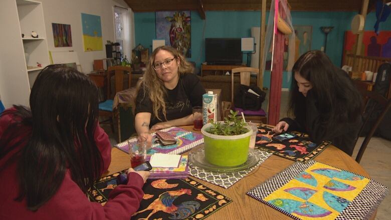 Three women sit a table with a jade plant in the middle.