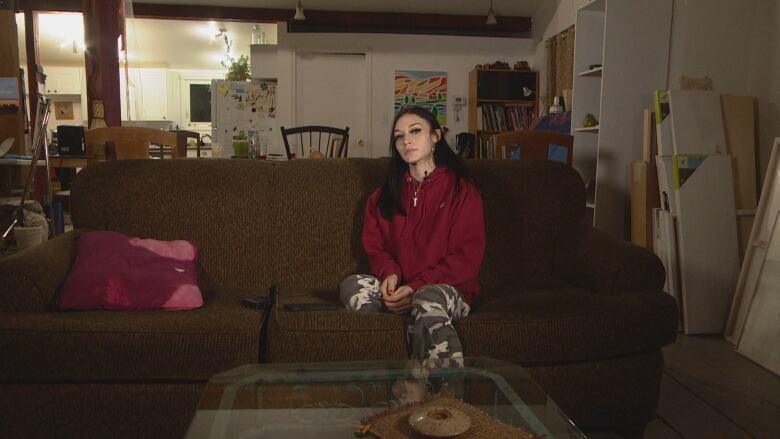 A girl clad in a maroon hoodie sits at the sofa.