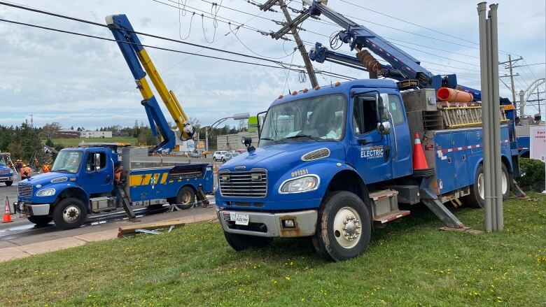 Two large blue utility trucks repairing power lines.