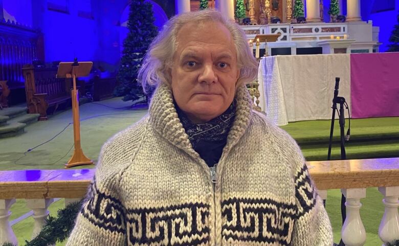 A man with long white hair stands in a church.