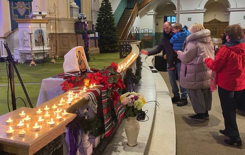 Several people lay small candles on a church altar.