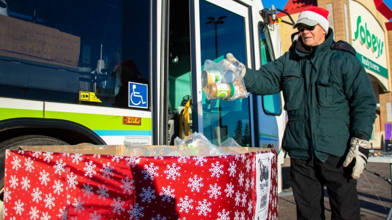 A man places food donations in a giant cardboard box wrapped like a present.