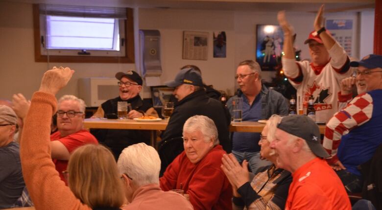 Fans in a bar cheer, some of them raising their arms in the air