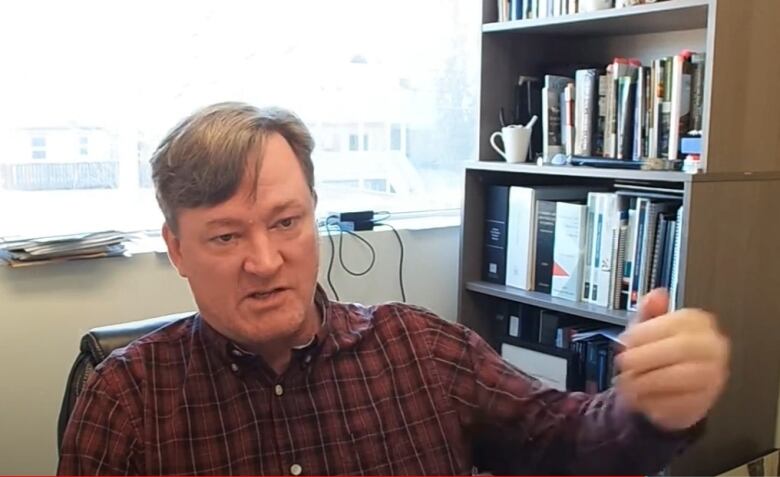 A man speaks to a camera sitting in an office.