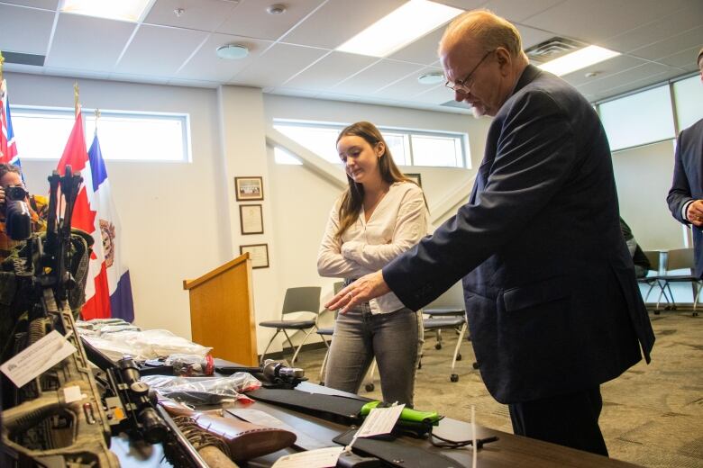 Two people look at illegal items displayed on a table after being seized by the police.