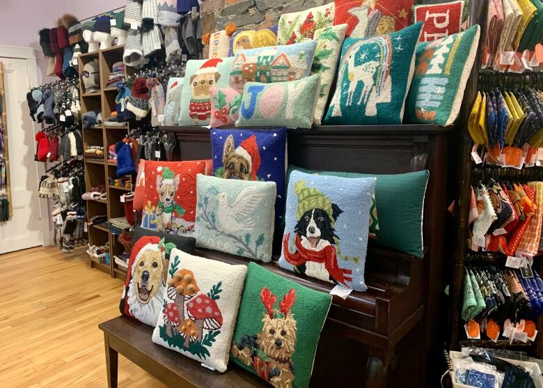 A variety of Christmas-themed pillows sit on a wooden display shelf.