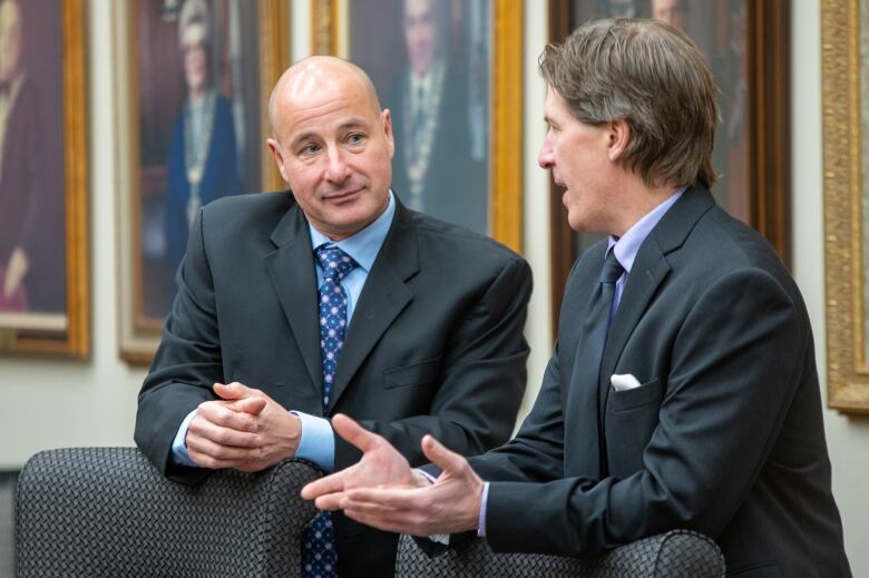 Two men in suits talk quietly to each other. 