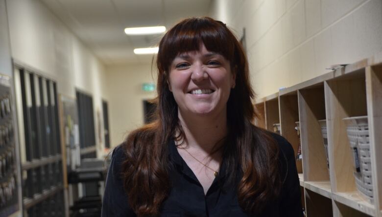 Cristina Scagnetti stands in a hallway with overhead fluorescent lights and cubbies with bins of children clothes next to her 