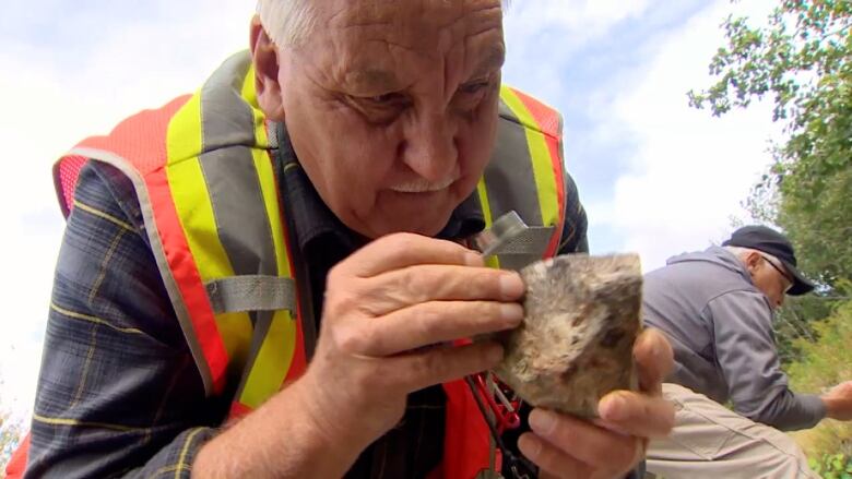 A man holds a rock in one hand and a small magnifying glass in the other.