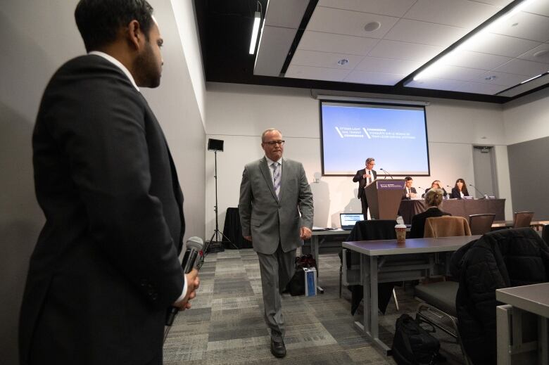 A man in a grey suit walks out of a media room.