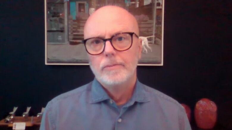 Dr. Michael Gardam stands in front of a painting and looks into a camera.