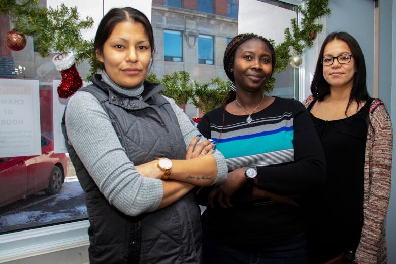 Three women stand in front of a window with Christmas decorations.