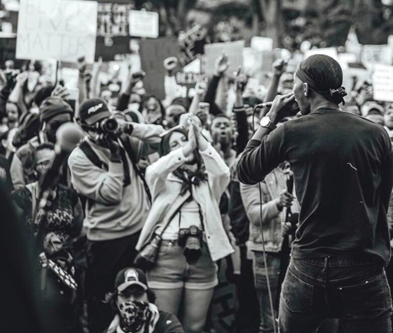 A black-and-white photo of a man speaking into a microphone in front of a large crowd.  