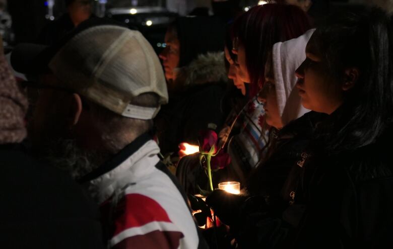 A person holds a rose in a crowd of people. Nearby, others hold candles.