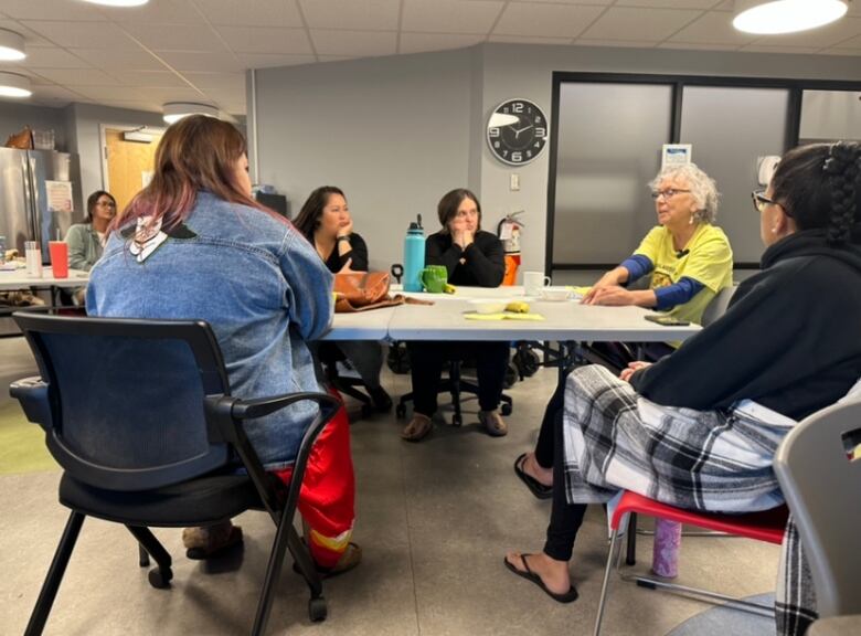 A group of women sit in chairs around a plastic table. They're focused on Elder Imelda Perley, who's sitting with them at the head of the table.