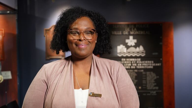 A smiling woman in foreground, Montreal police plaque on wall in background.