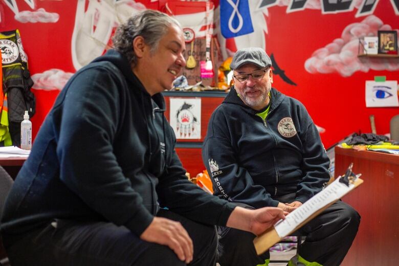 Two men sit smiling.