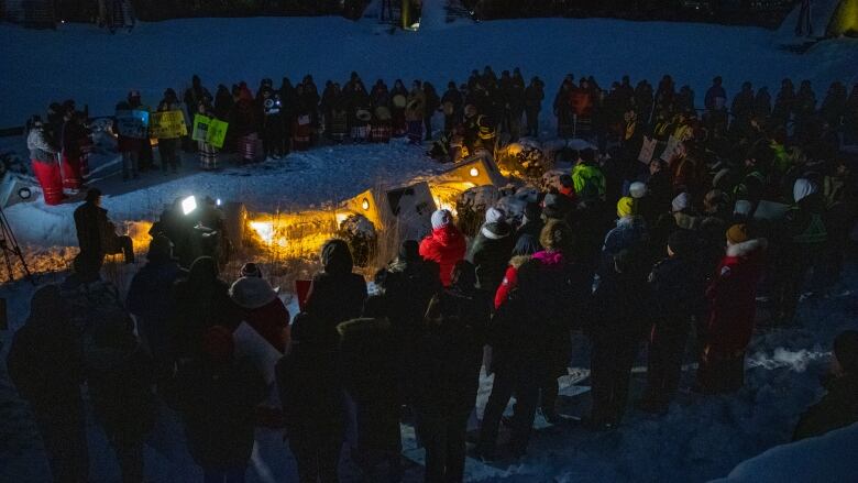 People gather for a candelit vigil on a dark night.