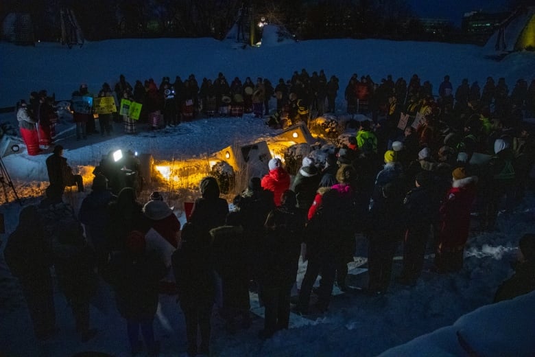 People gather for a candelit vigil on a dark night.