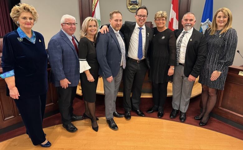 Eight people stand smiling in a small municipal council room.  