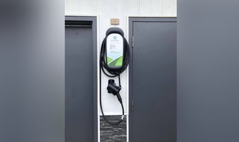 An electric vehicle charger hangs on the side of a building.