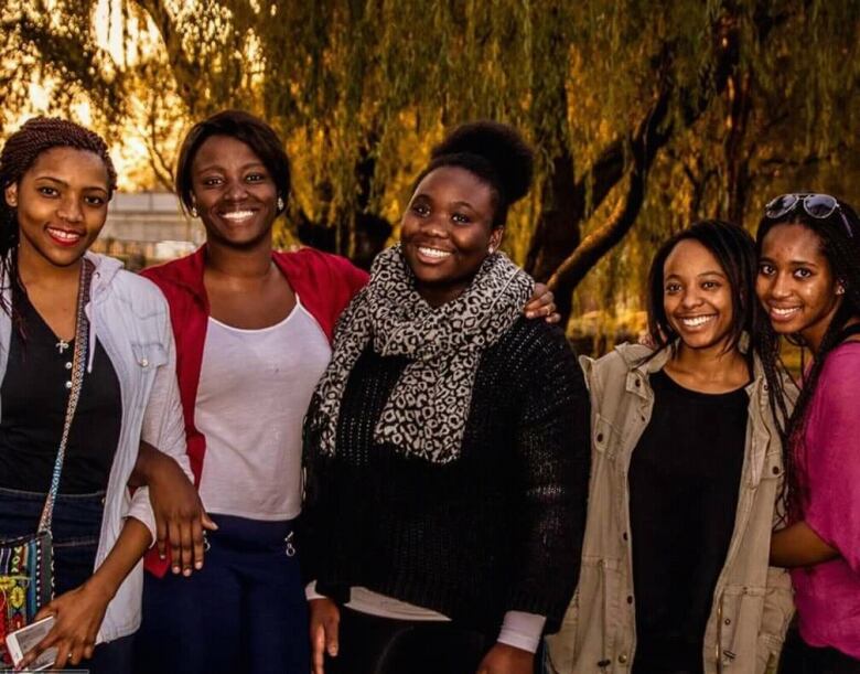 Five girls stand close together, some with their arms around each other. 