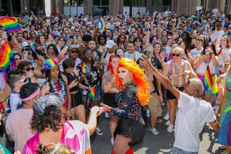 A person in bright clothing and makeup stands in a crowd.