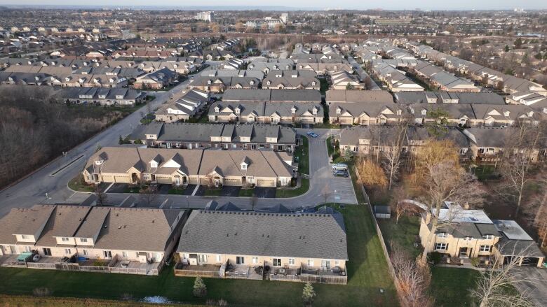 Many rows of matching subdivision houses are shown as far as the eye can see in a drone photo from the sky.