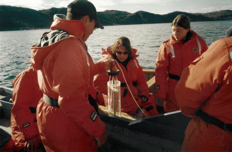 A group of people in orange overalls circle around a device to sample water.