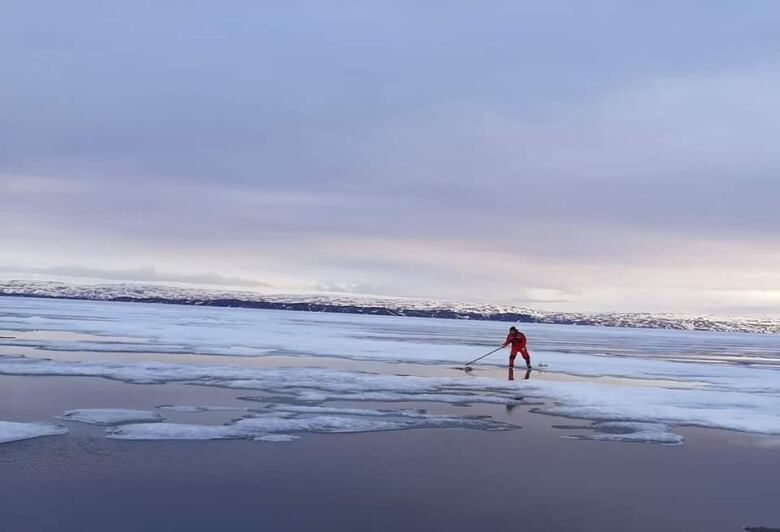 A distance shot of a man hunting a seal on the ice.