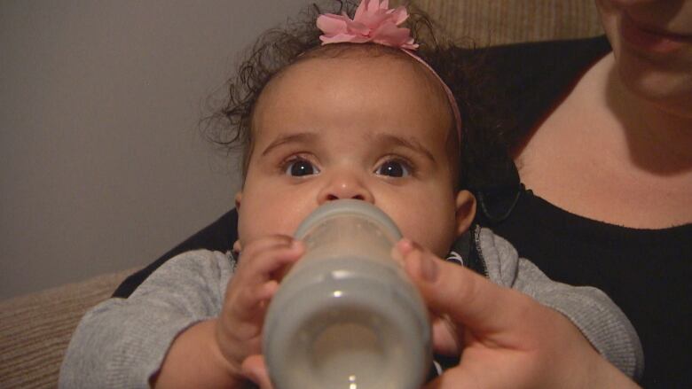 A baby in her mother's arms feeds while holding a bottle.