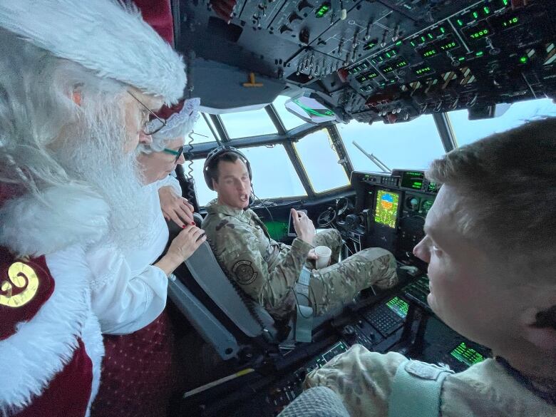 Santa Claus speaks with pilots aboard a plane.