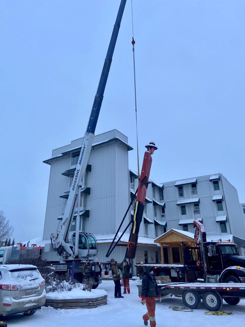 A crane lifting a 30 foot wooden statue into the air.