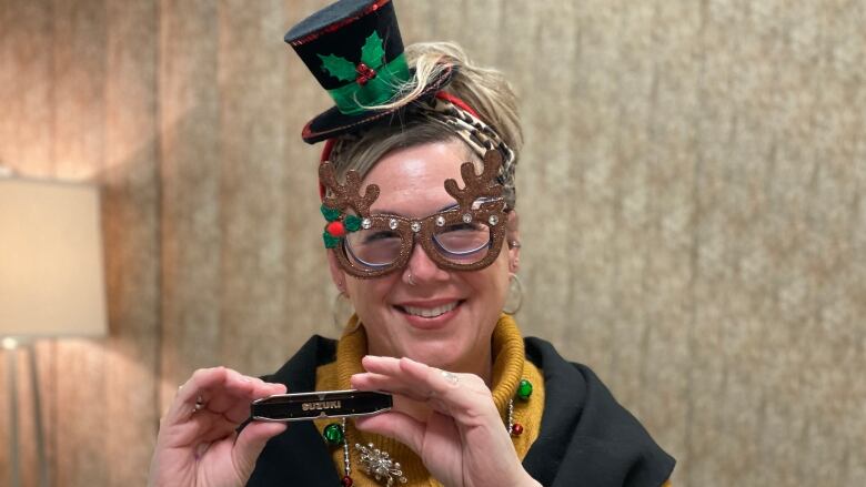 A smiling woman dressed in festive glasses and top hat holds a harmonica.