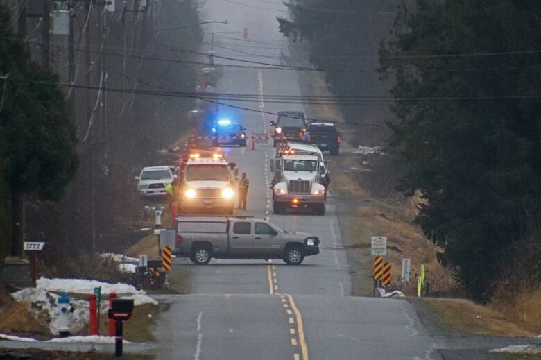 Police vehicles block a rural road.