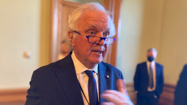 A man with white hair wearing glasses and blue suit and tie.