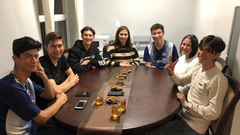 Seven siblings sit around their dining room table, smiling at the camera.