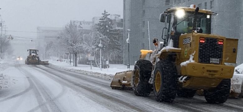 Two snow plows head toward each other on a snowy city street.