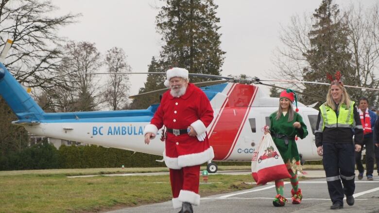 Santa, an elf and a paramedic with reindeer antlers walk away from a B.C. ambulance helicopter at the B.C. Children's Hospital.