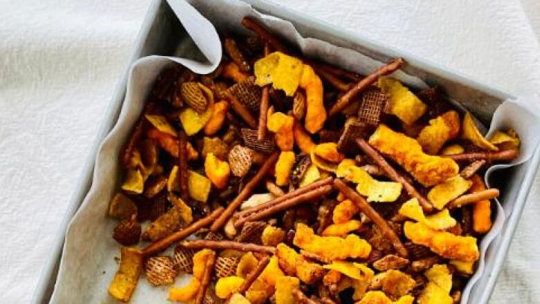 A baking tray full of different crackers, pretzels and crunchy items sits on a kitchen table.