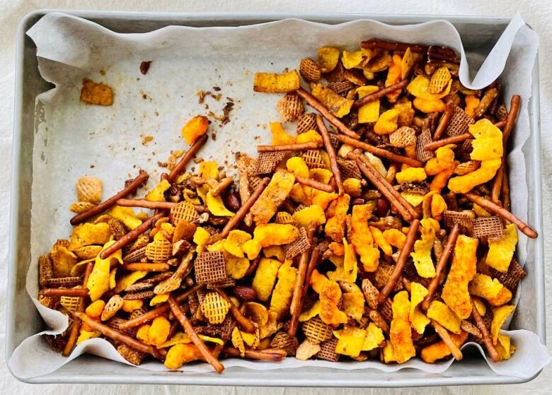 A tray of snack mix, lined with parchment paper, sits on a table.